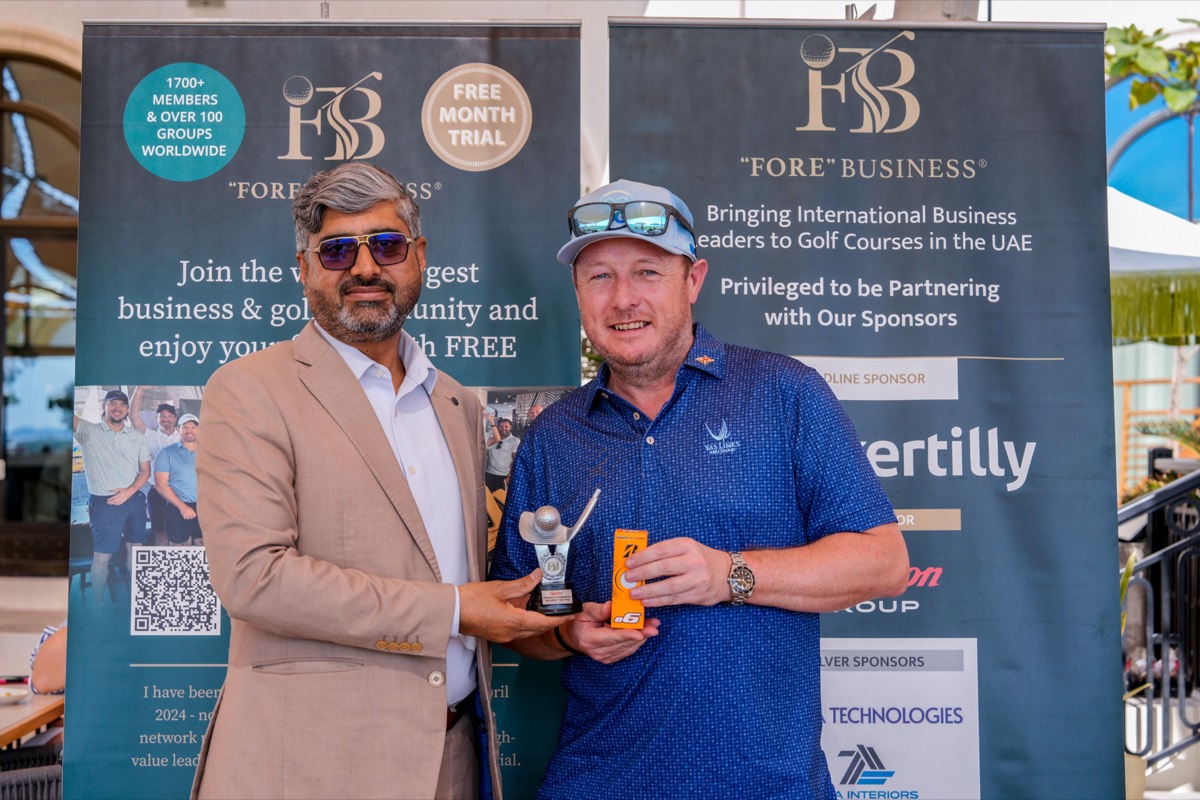 A member and a guest with a trophy in front of the "FORE" Business banners at Yas Links